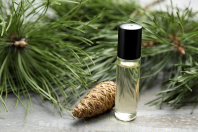 Photo of Pine essential oil, cone and branches on grey wooden table, closeup