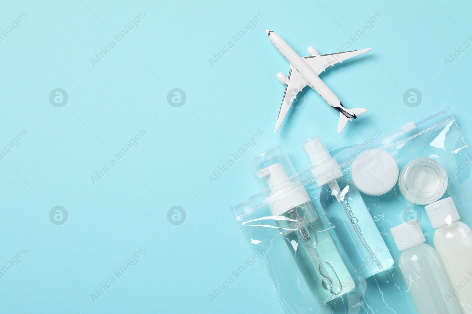 Photo of Cosmetic travel kit in plastic bag and toy plane on light blue background, top view with space for text. Bath accessories
