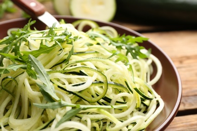 Photo of Tasty zucchini pasta with arugula on wooden table, closeup