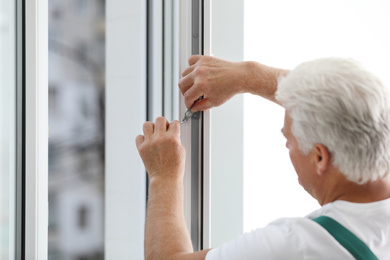 Mature construction worker repairing plastic window indoors