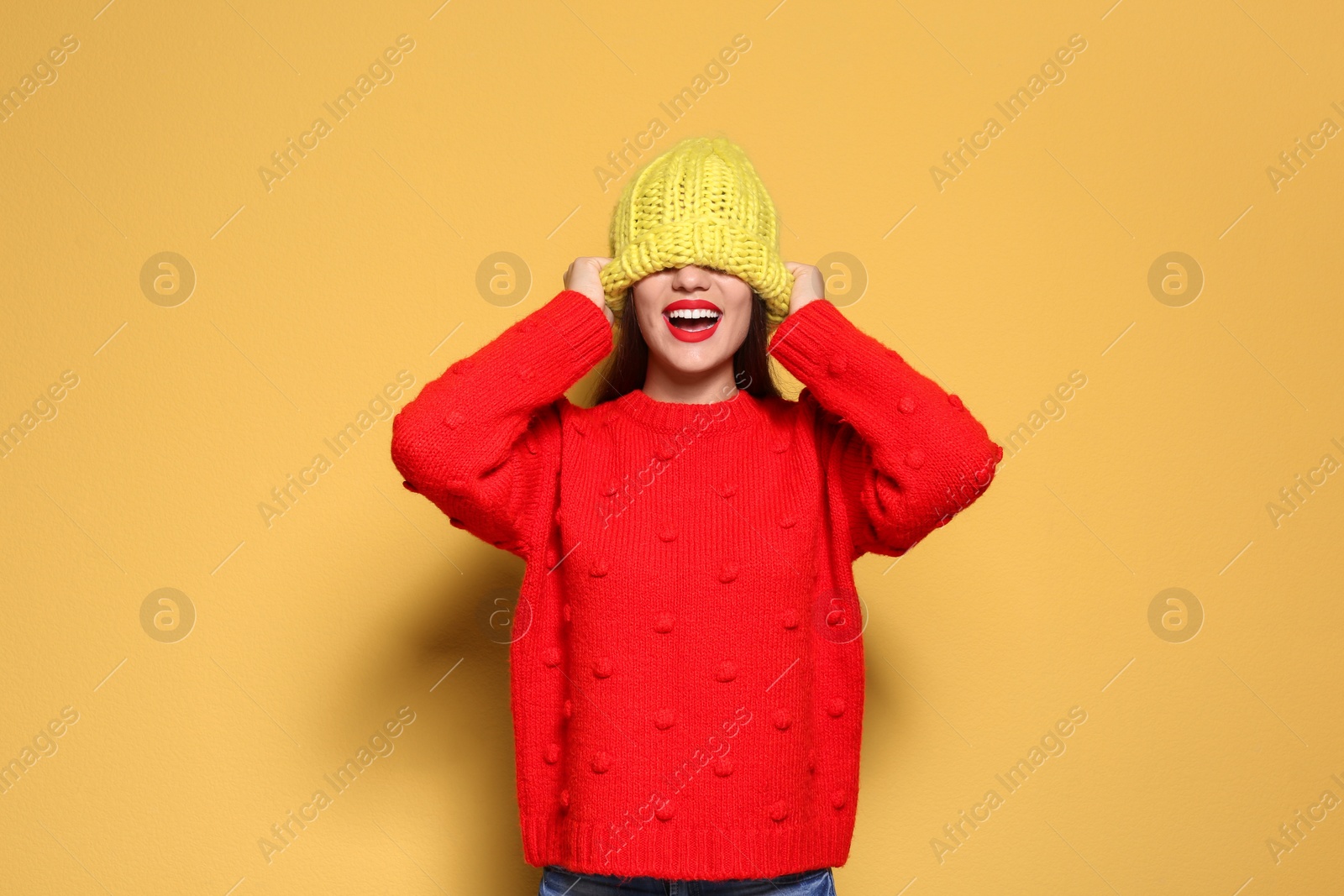 Photo of Young woman in warm sweater and knitted hat on color background. Celebrating Christmas