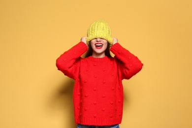 Young woman in warm sweater and knitted hat on color background. Celebrating Christmas