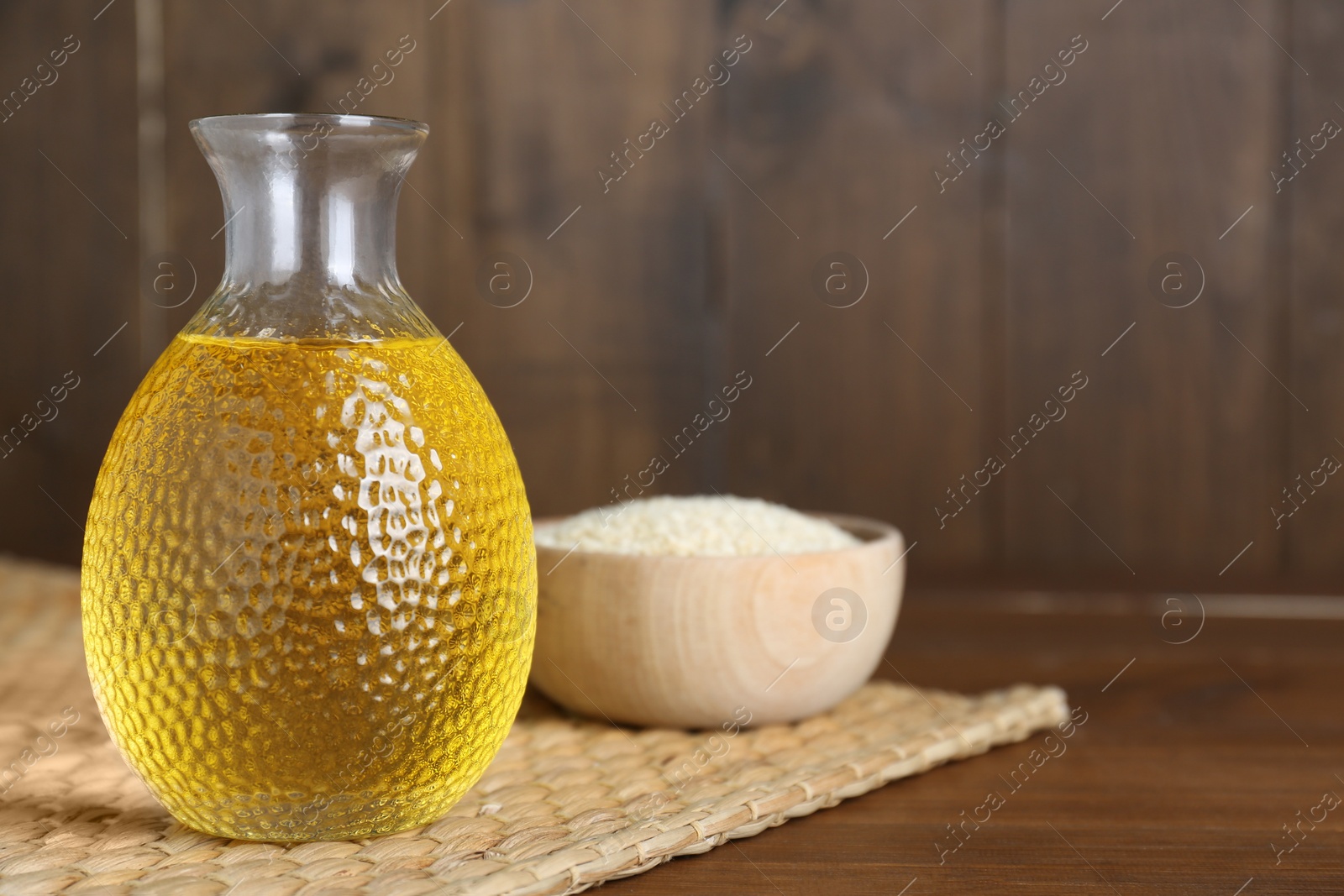 Photo of Fresh sesame oil and seeds on wooden table. Space for text