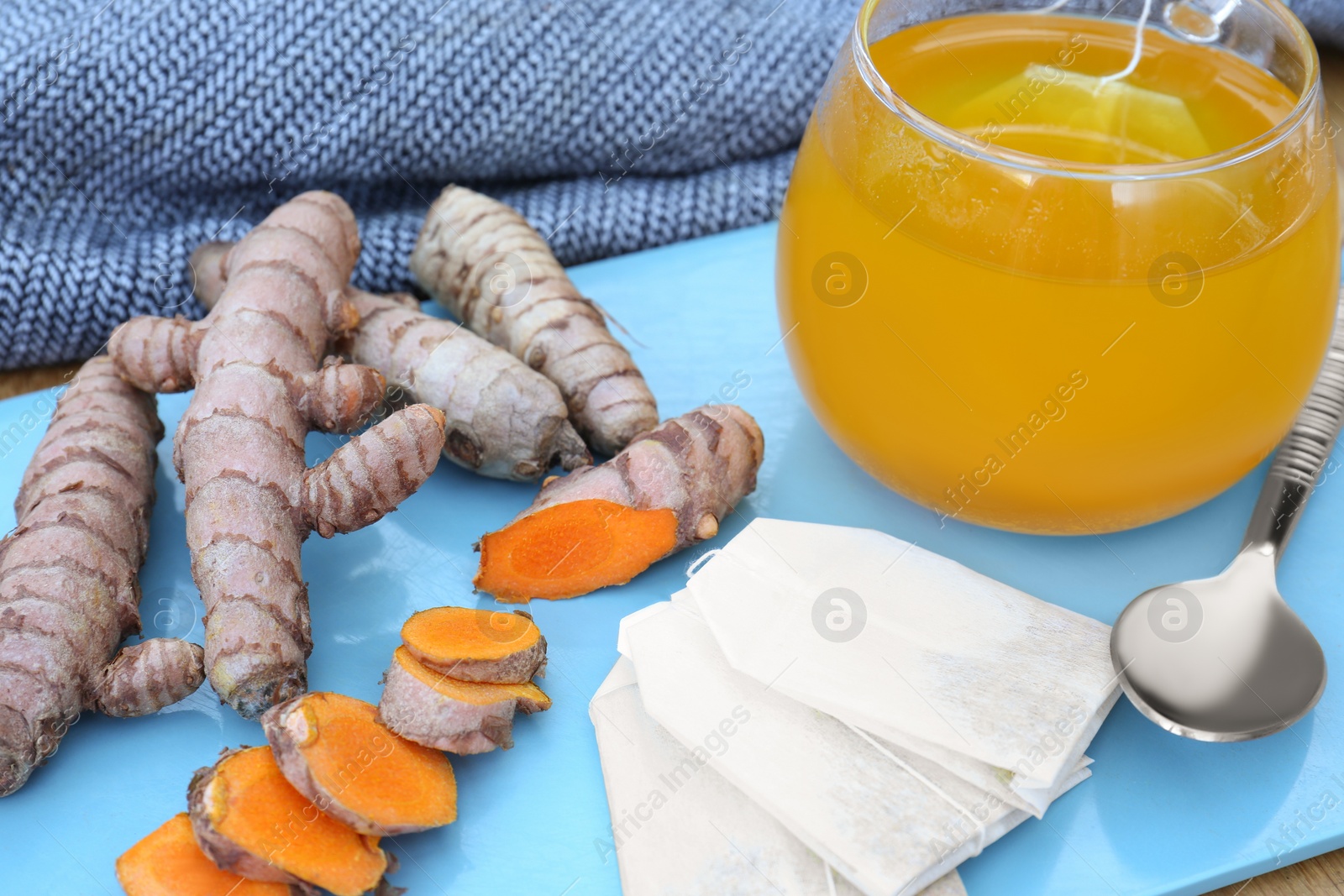 Photo of Glass cup with hot tea and turmeric roots on light blue tray