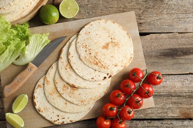 Photo of Tasty homemade tortillas, tomatoes, lime, lettuce and knife on wooden table, top view