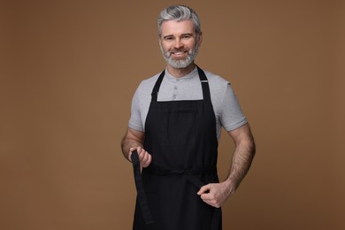 Photo of Happy man wearing kitchen apron on brown background. Mockup for design