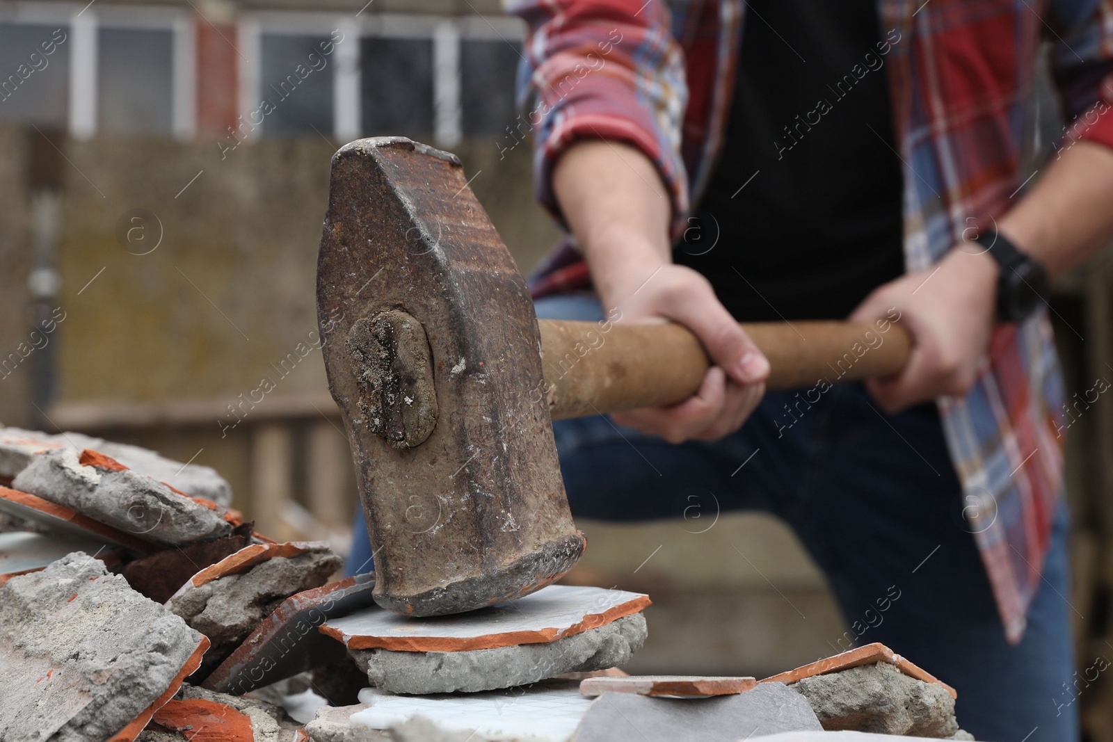 Photo of Man breaking bricks with sledgehammer outdoors, selective focus