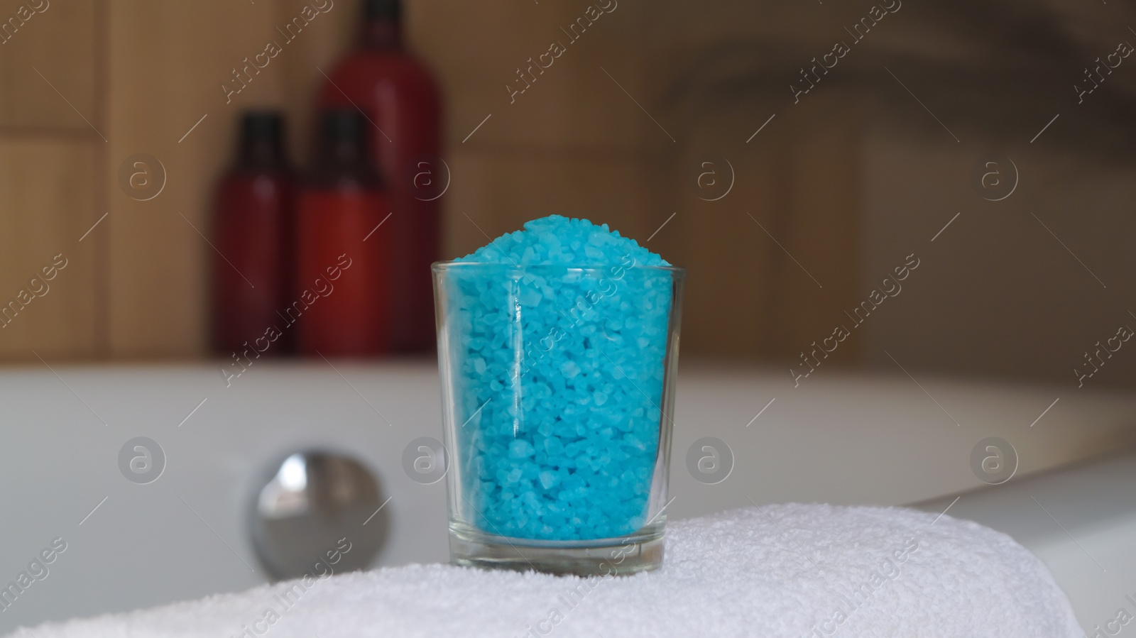 Photo of Glass with sea salt and fluffy towel on bath
