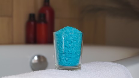 Photo of Glass with sea salt and fluffy towel on bath