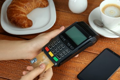Photo of Woman with credit card using modern payment terminal at wooden table, closeup