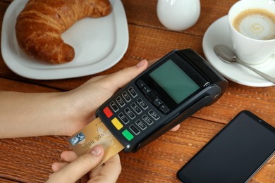 Woman with credit card using modern payment terminal at wooden table, closeup