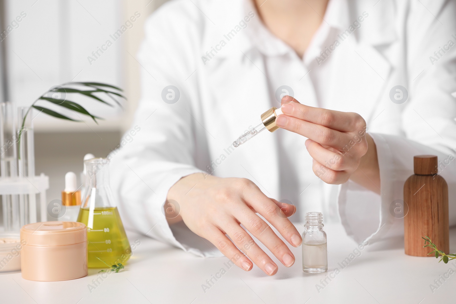 Photo of Dermatologist testing essential oil at white table indoors, closeup