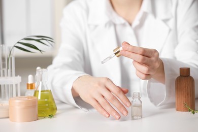 Photo of Dermatologist testing essential oil at white table indoors, closeup