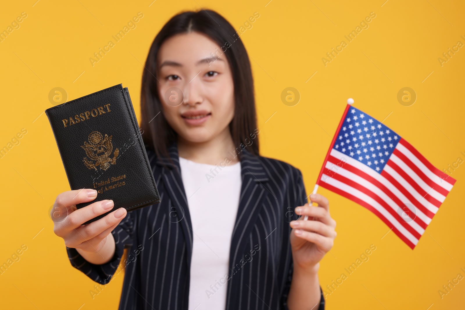 Photo of Immigration to United States of America. Woman with passport and flag on orange background, selective focus