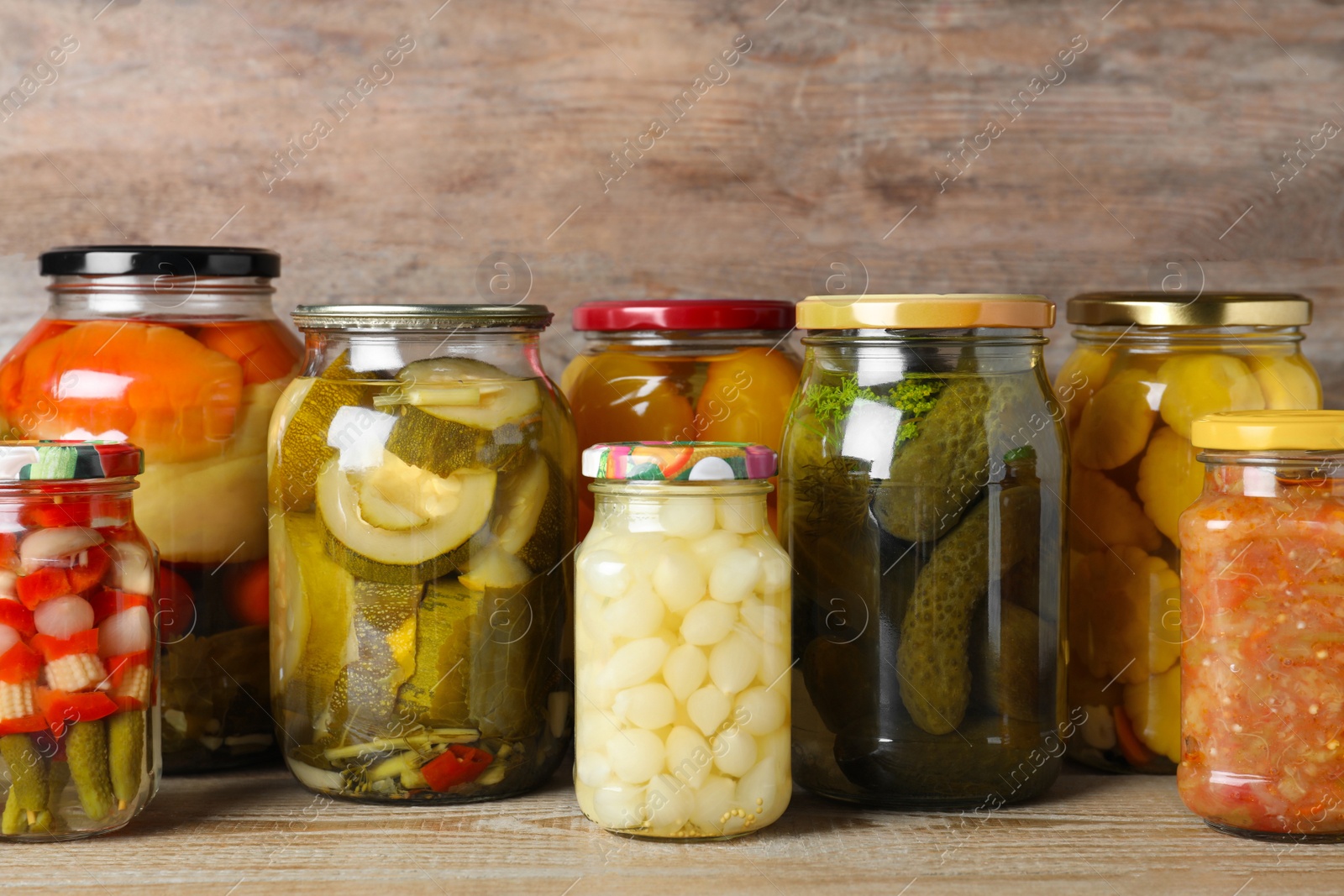 Photo of Jars with pickled vegetables on wooden table against brown background