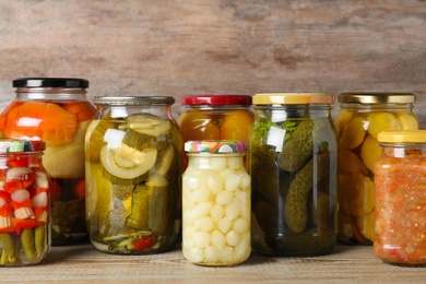 Photo of Jars with pickled vegetables on wooden table against brown background