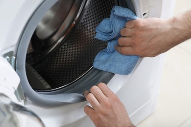 Photo of Man cleaning empty washing machine with rag, closeup