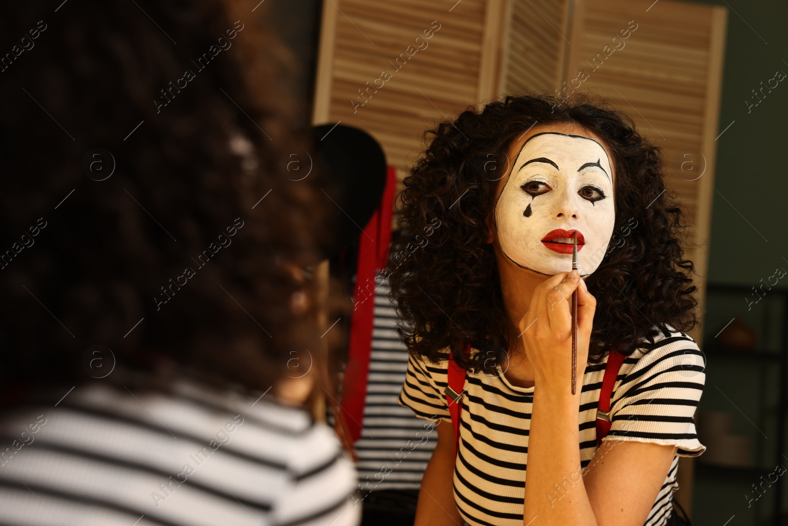 Photo of Young woman applying mime makeup near mirror indoors