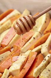 Photo of Pouring honey onto slices of parsnip and carrot, closeup