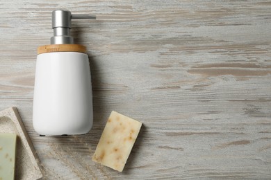 Soap bars and dispenser on wooden table, flat lay. Space for text