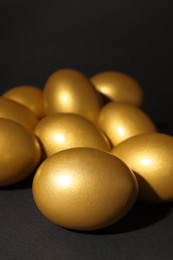 Photo of Many shiny golden eggs on black background