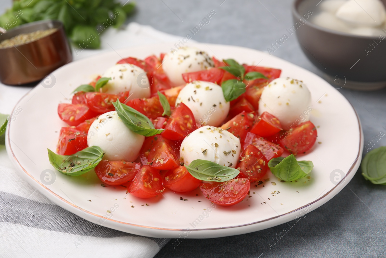 Photo of Tasty salad Caprese with tomatoes, mozzarella balls and basil on grey table, closeup
