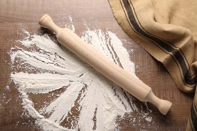 Photo of Scattered flour and rolling pin on wooden table, top view