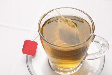 Photo of Tea bag in cup with hot drink on white table, closeup