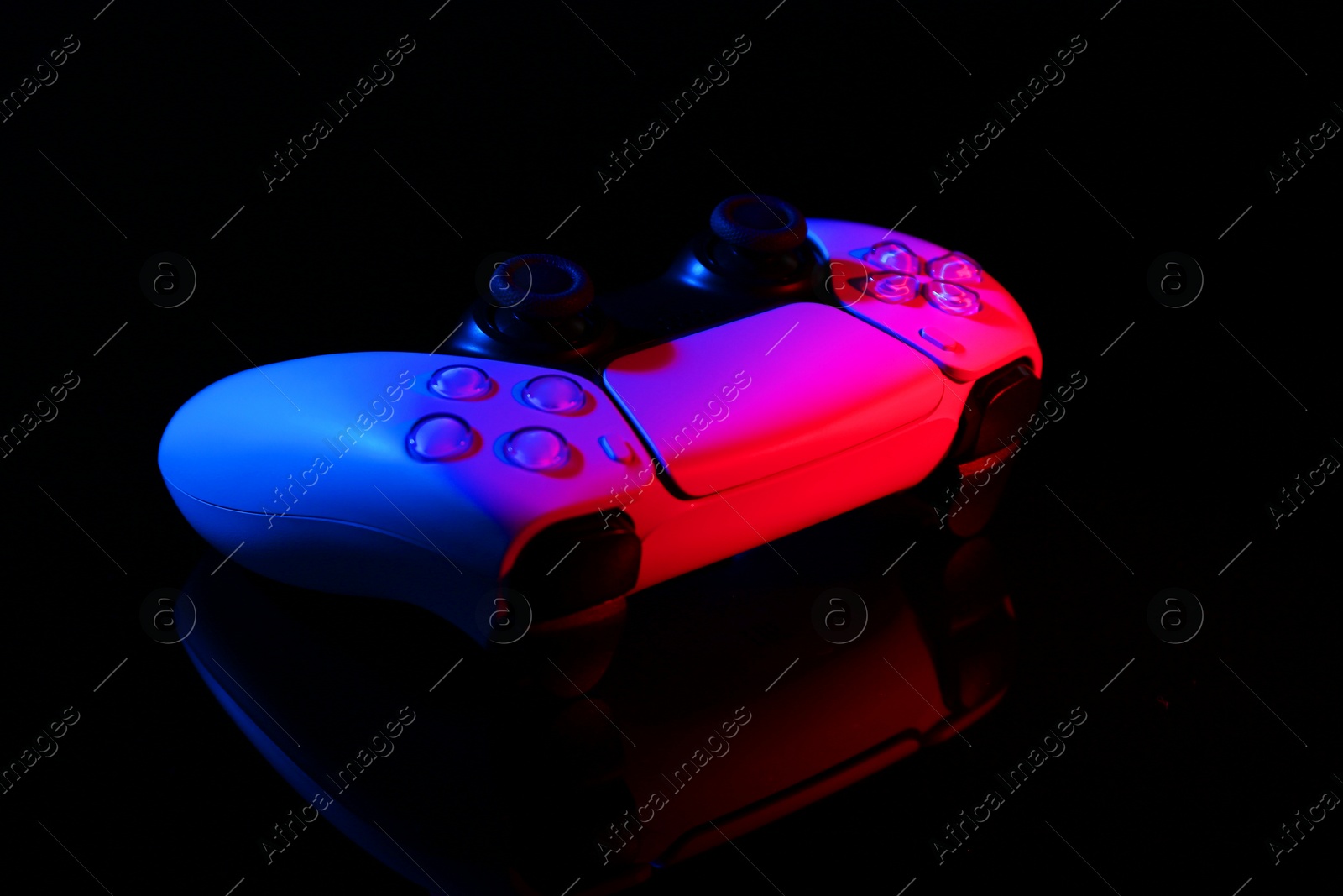 Photo of Wireless game controller on black mirror surface in neon lights