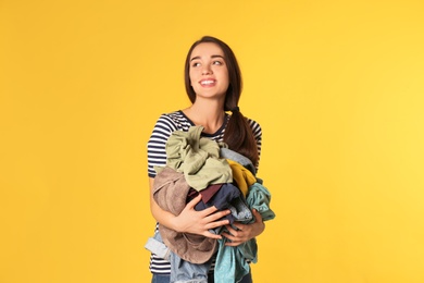 Photo of Happy young woman holding pile of dirty laundry on color background