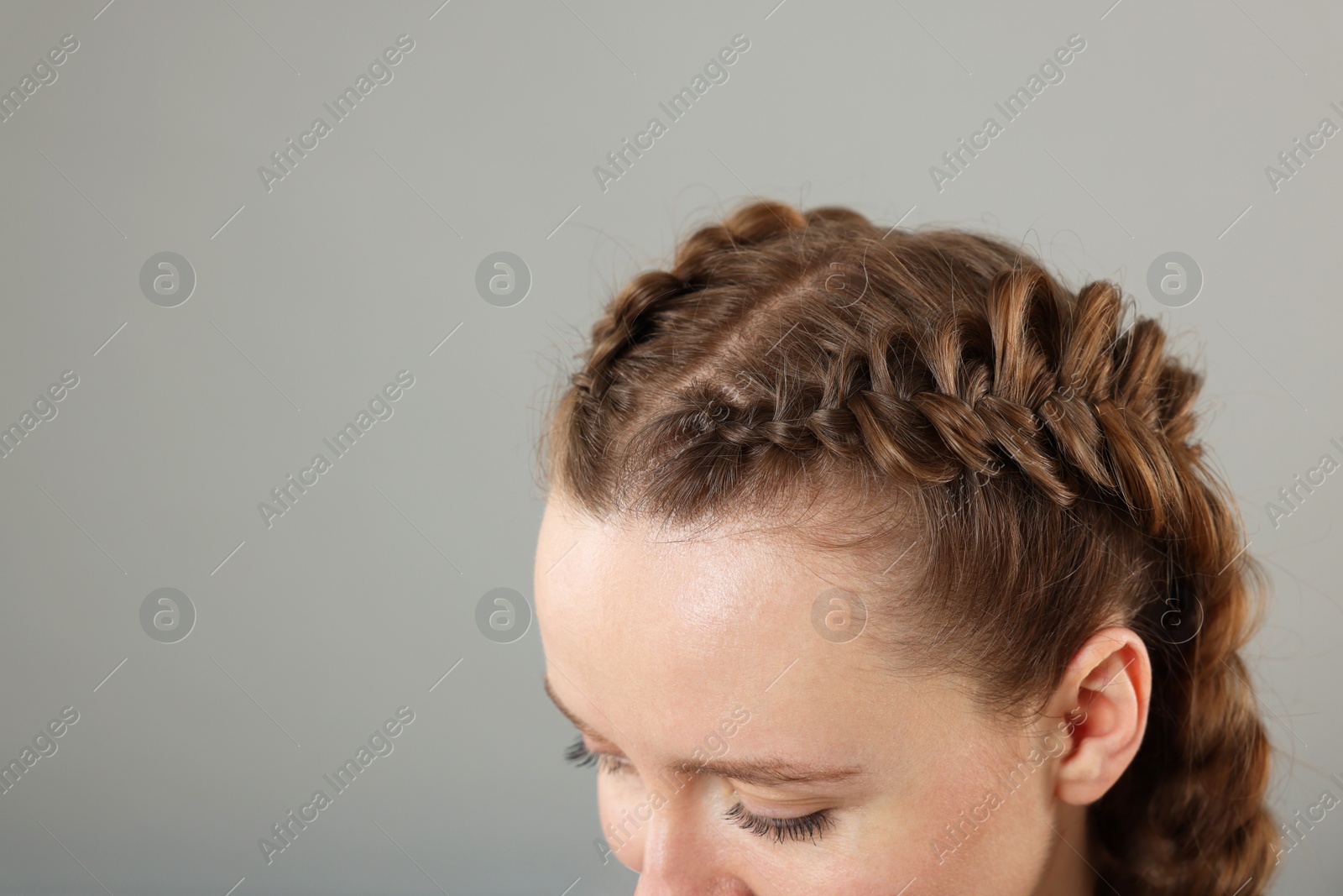 Photo of Woman with braided hair on grey background, closeup. Space for text