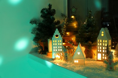 Photo of Christmas atmosphere. Beautiful glowing houses, fir trees and toys on window sill indoors. Space for text