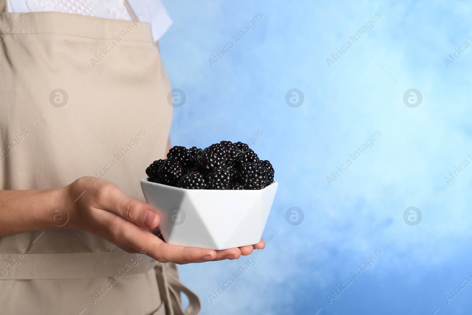 Photo of Woman holding bowl of fresh blackberry against color background. Space for text