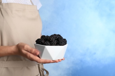 Photo of Woman holding bowl of fresh blackberry against color background. Space for text