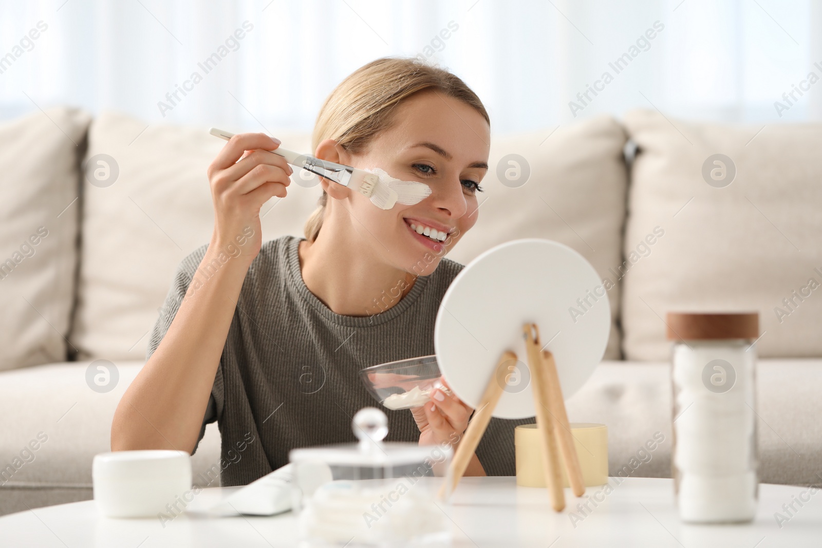 Photo of Young woman applying face mask in front of mirror at home. Spa treatments