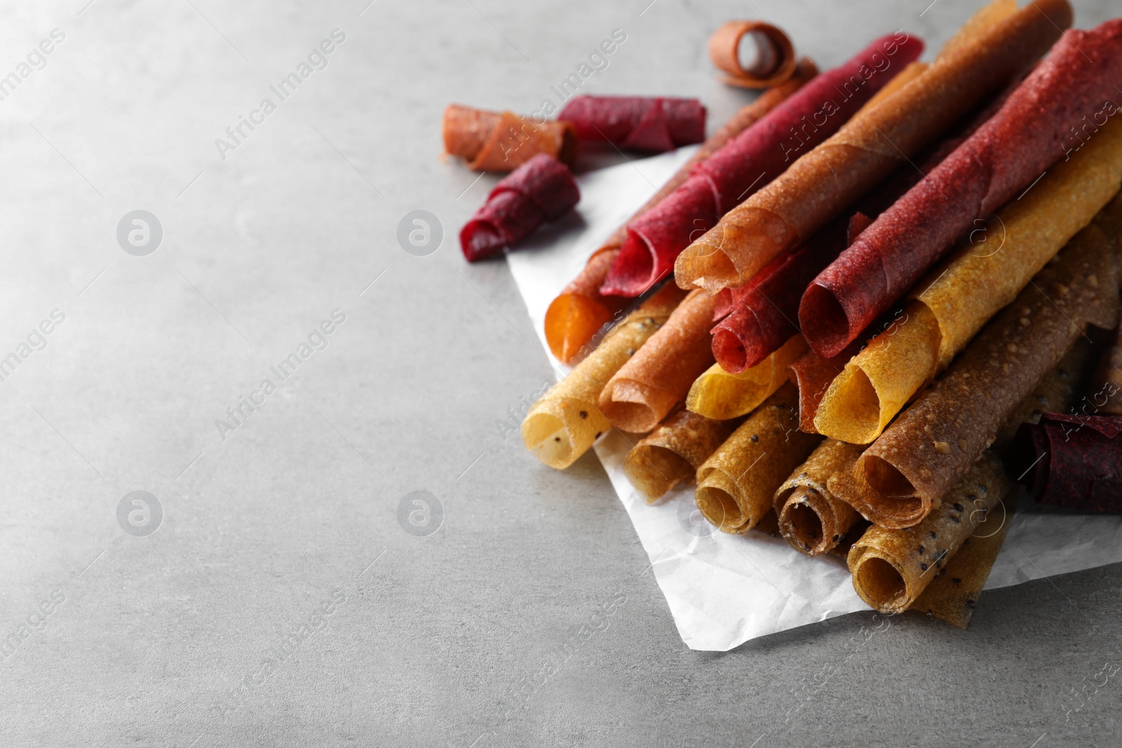 Photo of Delicious fruit leather rolls on grey table. Space for text