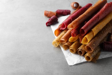 Photo of Delicious fruit leather rolls on grey table. Space for text