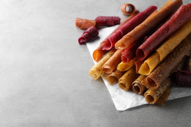 Delicious fruit leather rolls on grey table. Space for text