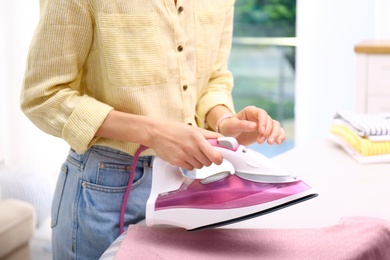 Photo of Young woman ironing clean laundry indoors, closeup