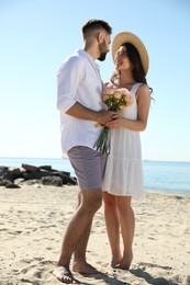 Photo of Happy young couple with flowers on beach near sea. Honeymoon trip