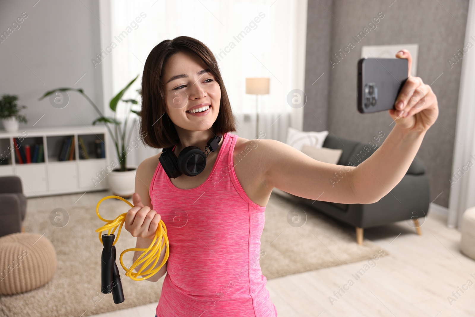 Photo of Happy sports blogger holding skipping rope while streaming online fitness lesson with smartphone at home