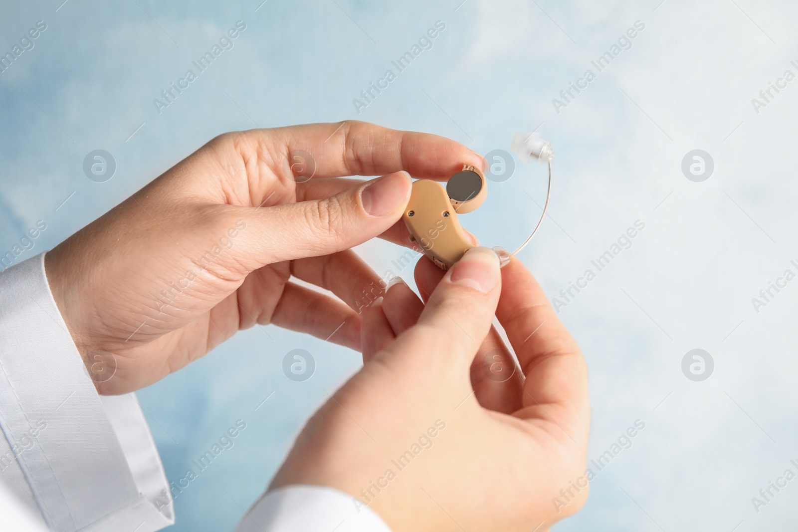 Photo of Woman putting battery into hearing aid on light background, closeup