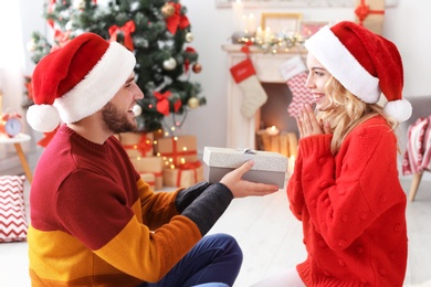 Photo of Young couple in Santa hats with Christmas gift at home