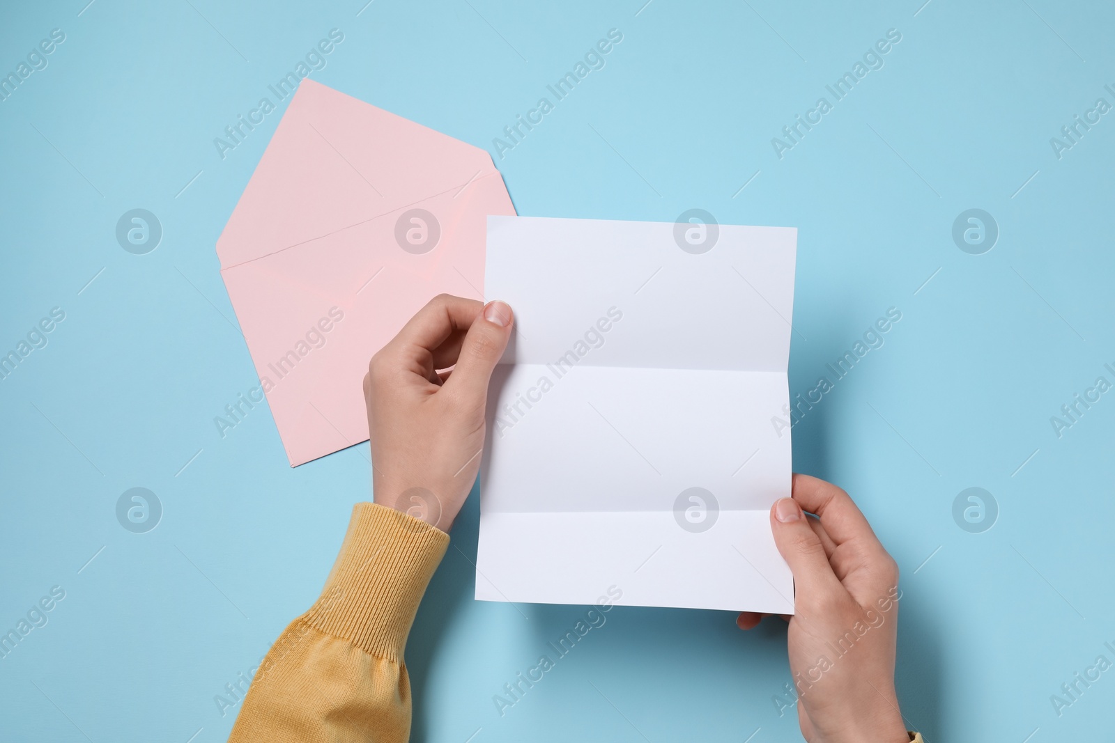 Photo of Woman with blank sheet of paper at light blue table, top view. Space for text