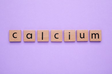 Word Calcium made of wooden cubes with letters on violet background, top view