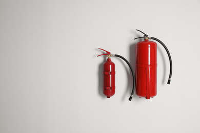 Different fire extinguishers hanging on white wall. Space for text