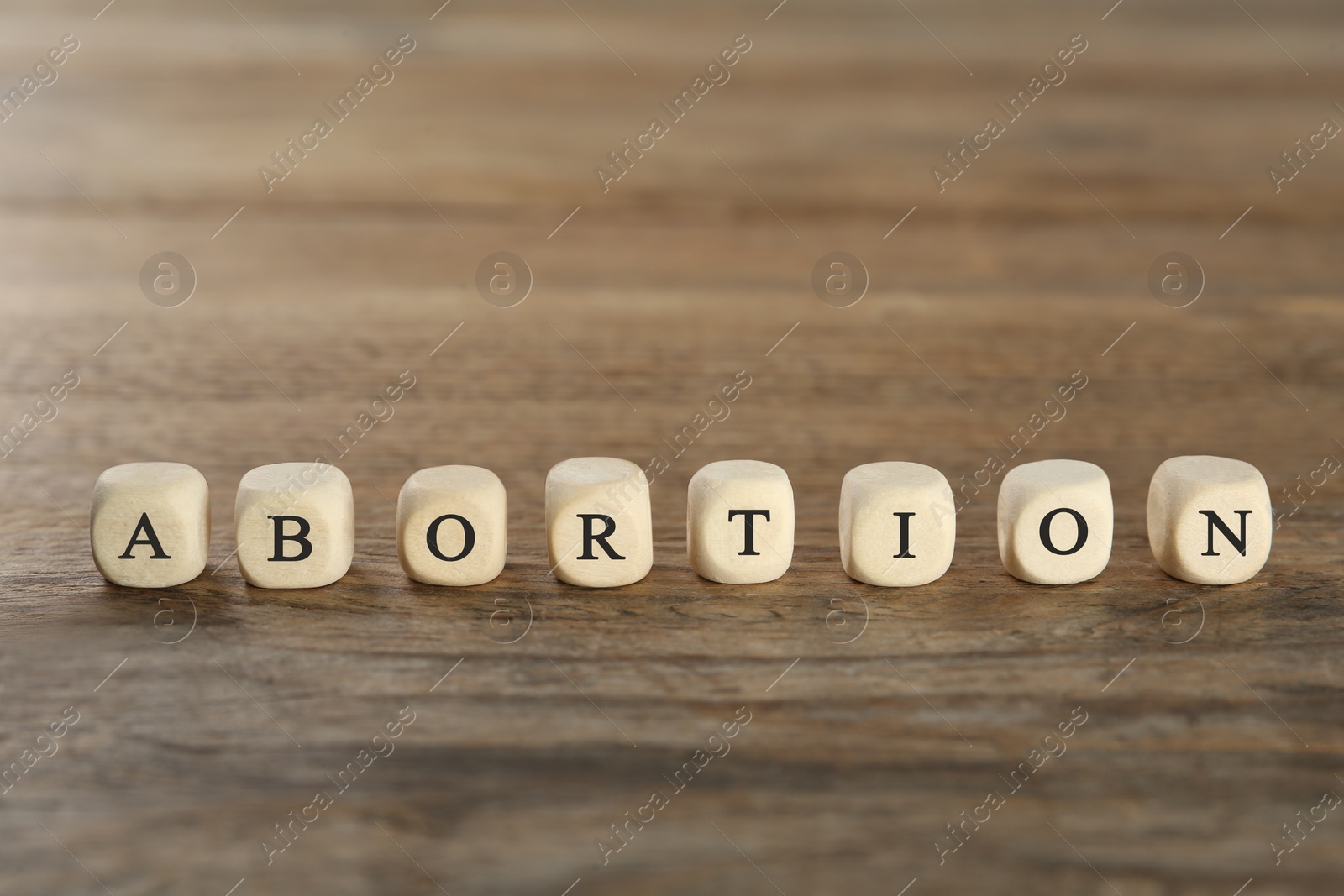 Photo of Word Abortion made of cubes on wooden table, closeup