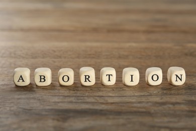 Photo of Word Abortion made of cubes on wooden table, closeup