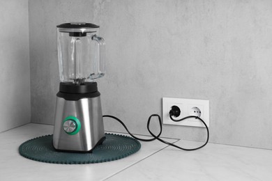 Electric blender plugged into power socket on white table