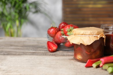 Photo of Tasty rhubarb jam, stems and strawberries on wooden table. Space for text